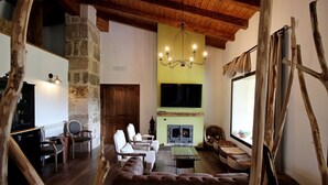 A cozy living room with a stone wall, a fireplace, a television, and a large window. - Hotel Rural San Giles (Aldeanueva de la Vera)