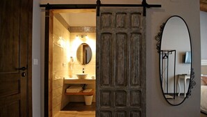 A bathroom with a wooden door, a sink, a mirror, and a towel rack. - Hotel Rural San Giles (Aldeanueva de la Vera)
