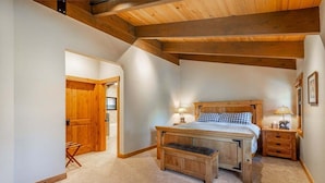 Un dormitorio con una cama de madera, una mesita de noche, un banco y una puerta que da a otra habitación.