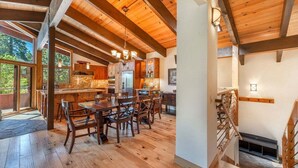 Una cocina amplia con vigas de madera, un comedor con una mesa grande y sillas, y una escalera que lleva a un nivel superior.