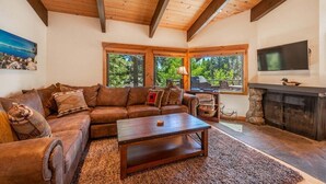 Una sala de estar acogedora con techo de madera, chimenea, televisor y un ventanal con vistas a árboles.