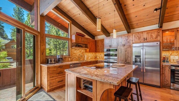 Una cocina moderna con armarios de madera, una isla grande, electrodomésticos de acero inoxidable y ventanas amplias.