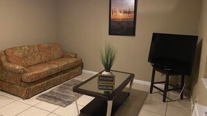 A living room with a sofa, a coffee table with a welcome sign, a television, and a framed picture on the wall. - JLS Apartments Comples (Vero Beach)