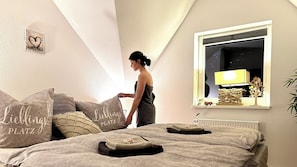 Une chambre à coucher avec un lit, des oreillers, une table de chevet, une lampe et une fenêtre.
