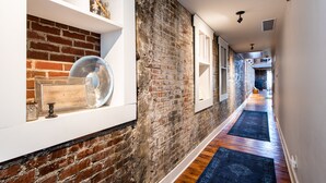 A hallway with exposed brick walls, wooden flooring, and built-in shelves displaying decorative items. - Quaint Historic Downtown: Walk to Dinner & Shops, Poker Table, Rooftop, Garage (New Albany)