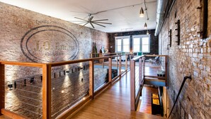 A spacious interior with exposed brick walls, wooden flooring, and a mezzanine level with a railing. - Quaint Historic Downtown: Walk to Dinner & Shops, Poker Table, Rooftop, Garage (New Albany)