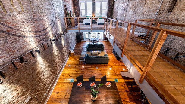 A loft-style room with a wooden floor, a dining table with chairs, and a sofa. There is a staircase connecting to an upper level. - Quaint Historic Downtown: Walk to Dinner & Shops, Poker Table, Rooftop, Garage (New Albany)
