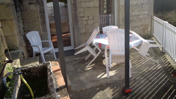 Edificio de piedra con un patio que tiene una mesa y sillas de plástico blanco.