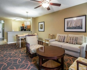 A hotel room with a dining area, a sofa set, a round table, and a ceiling fan.