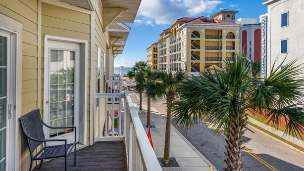 A balcony with a chair, a palm tree, and a building with balconies in the background. - motley crew , when you need the space for your big group of personalities  (Myrtle Beach)