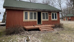 Eine kleine, eingeschossige Hütte mit einem grünen Dach, einer Haustür und einer kleinen Veranda.