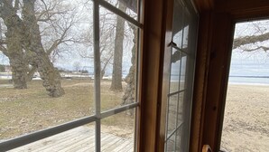 Ein Zimmer mit großem Fenster, das auf eine Holzterrasse und eine begrünte Fläche mit Bäumen blickt.