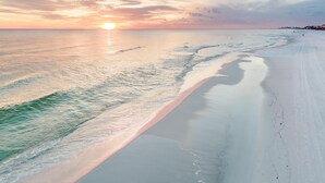 Une plage, un ciel dégagé et le soleil se couchant à l’horizon.