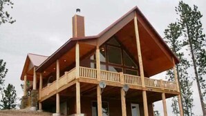 A large, multi-story wooden building with a balcony, large windows, and a chimney.