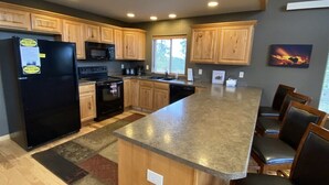 A kitchen with wooden cabinets, a black refrigerator, a microwave, and a large island with chairs.