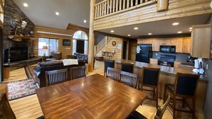 A spacious living area with a large wooden dining table, a fireplace, and a lofted kitchen area.