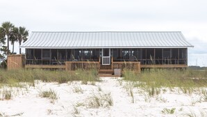 Ein Strandhaus mit Metalldach, großen Fenstern und einer Holzterrasse.