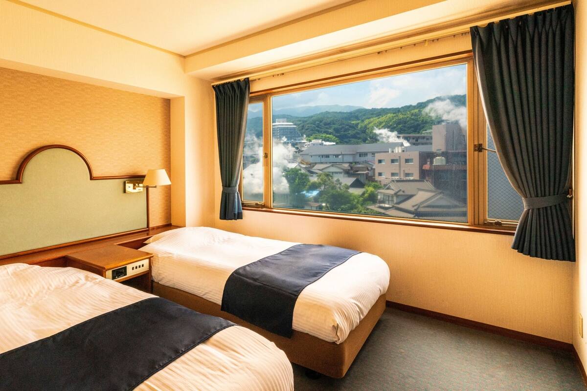 A hotel room with two beds, a view of a cityscape, and a window with curtains.