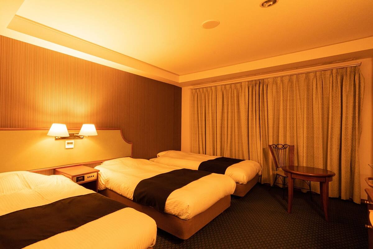 A hotel room with two beds, a nightstand, a chair, and a large window with curtains.
