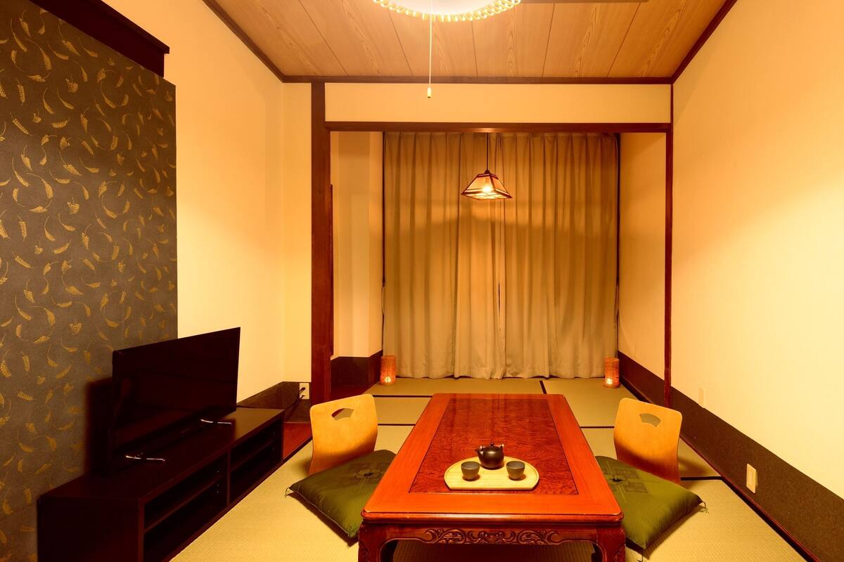 A traditional Japanese-style room with tatami flooring, a low table with a tea set, a television, and sliding doors.
