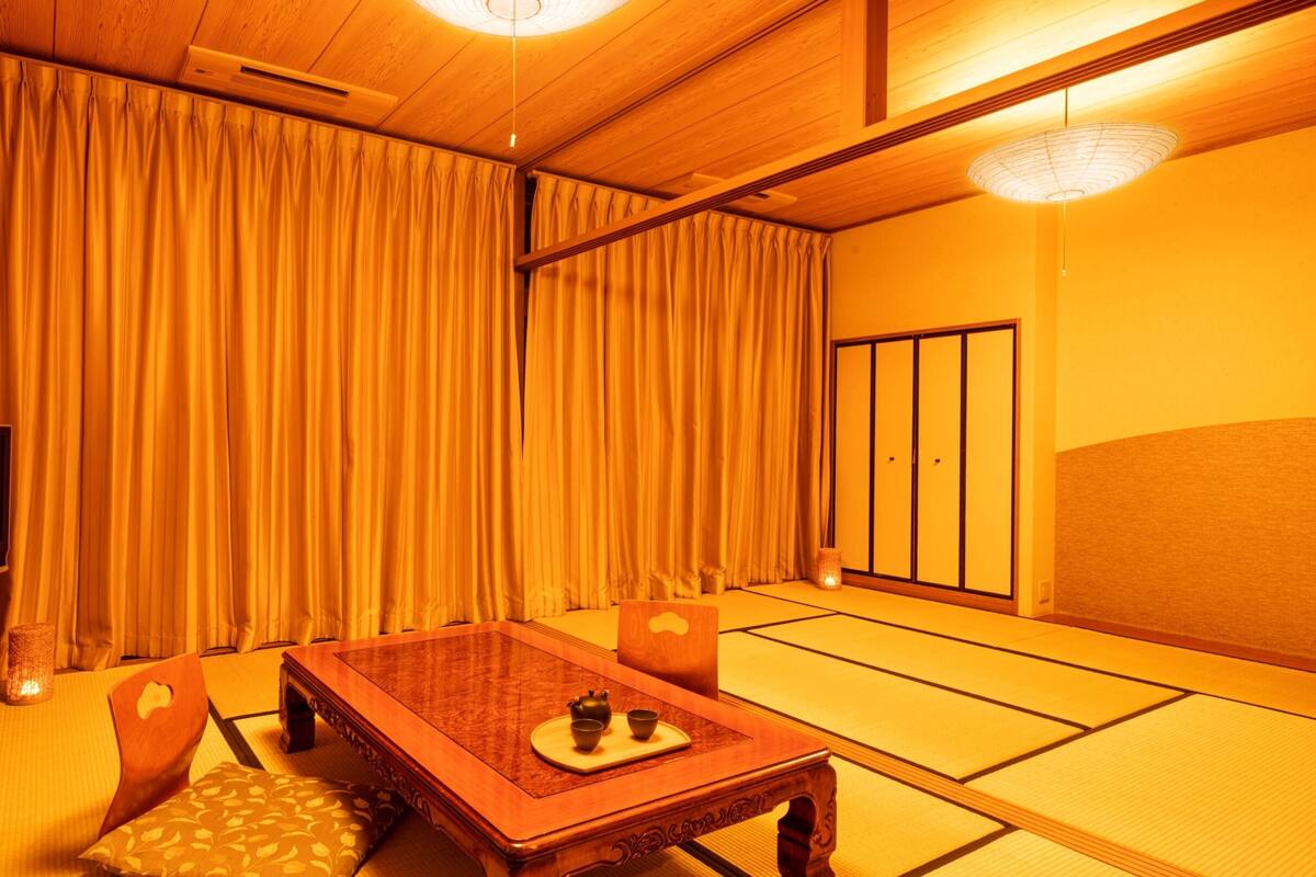 A traditional Japanese room with tatami flooring, a low wooden table with tea set, a television, and sliding doors.