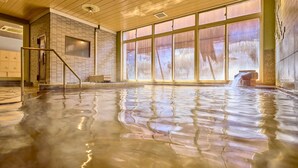 En inomhuspool med klart vatten, ett träpanelat tak och stora fönster.