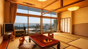 Ett traditionellt japanskt rum med tatamimattor på golvet, ett lågt träbord, en tv och utsikt över stadsbilden genom stora fönster.