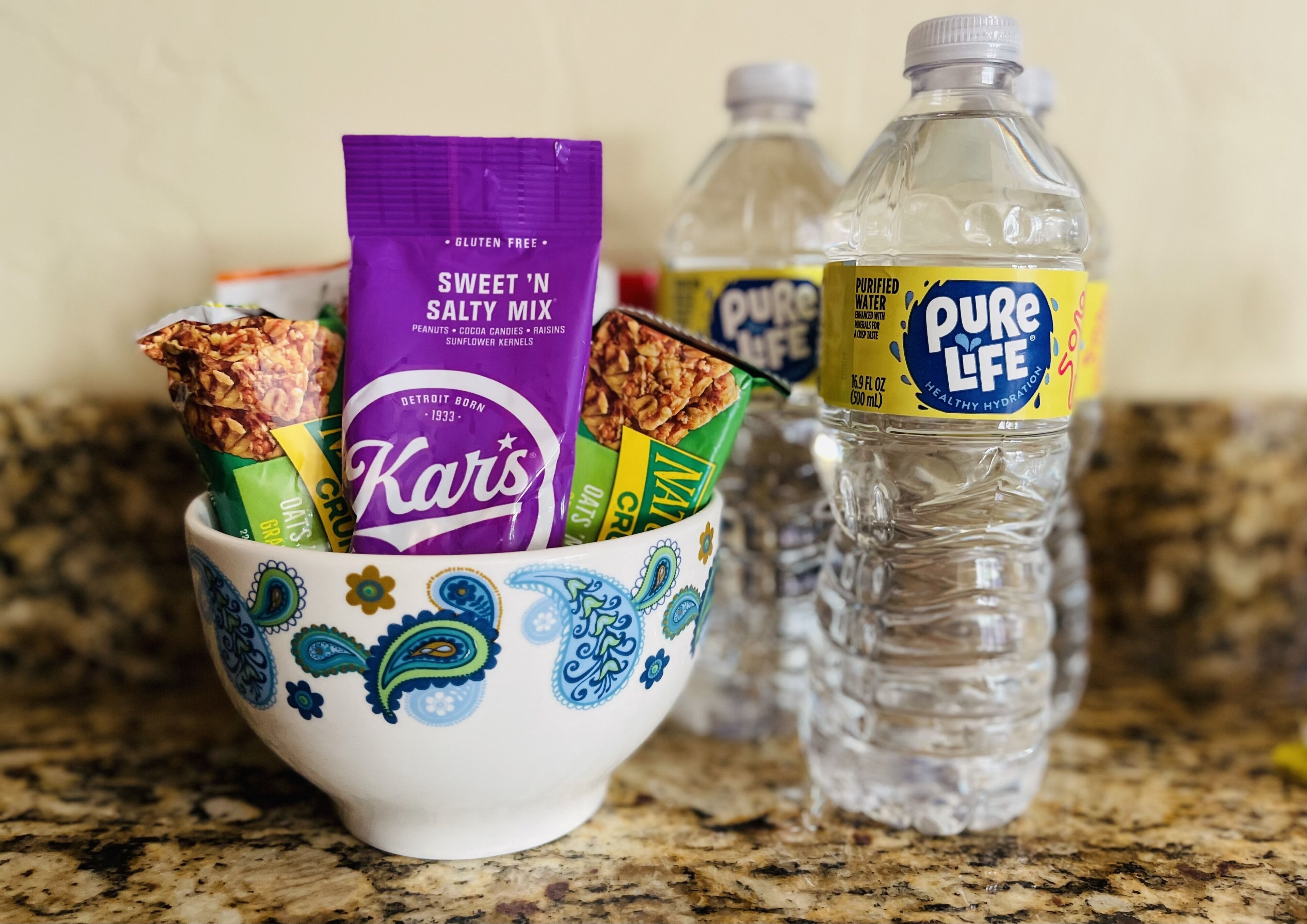 A bowl containing snacks and a water bottle on a granite countertop.