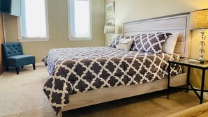 Une chambre à coucher avec un lit, une chaise, deux fenêtres, une lampe et un tableau au mur.