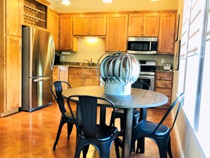 A kitchen with wooden cabinets, stainless steel appliances, and a round dining table with four chairs. - Aermotor Loft -100yds to Main Street! Sleeps 4, HOT TUB (Fredericksburg)