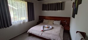 A bedroom with a bed, curtains, a headboard, and a wall-mounted air conditioner.