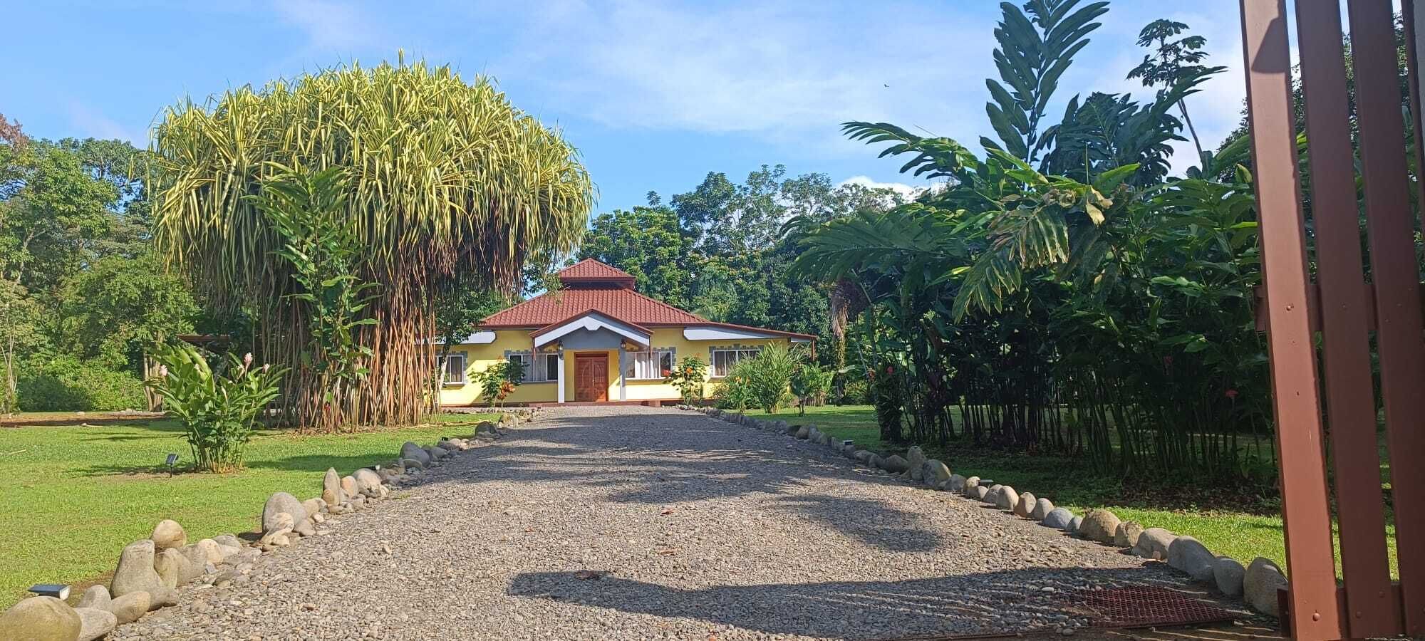 A house with a red roof, surrounded by a gravel driveway, and lush greenery.