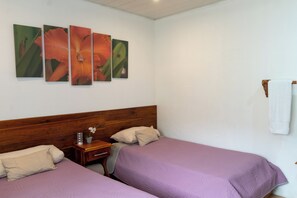 A bedroom with two beds, a wooden headboard, a nightstand, and a wall-mounted artwork.