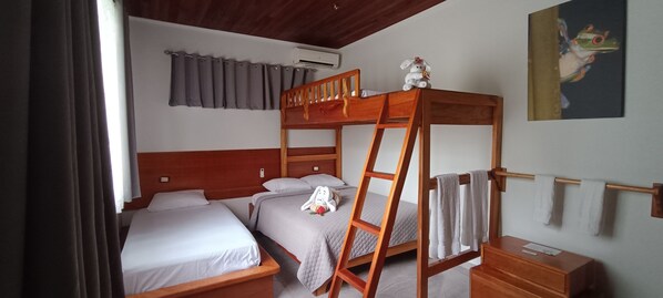 A room with two beds, a bunk bed, a ladder, a wooden dresser, a radiator, and a painting on the wall.