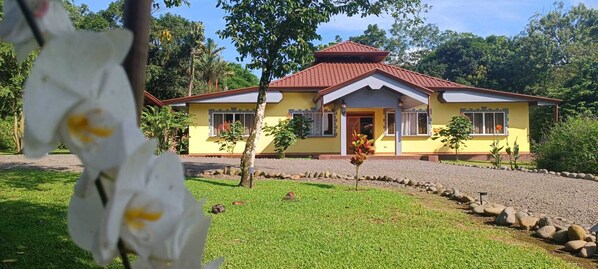 A yellow building with a red roof, surrounded by a well-maintained lawn and a gravel path.