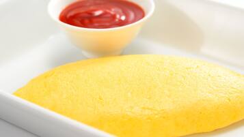 Une assiette blanche avec une omelette pliée et un petit bol de ketchup.