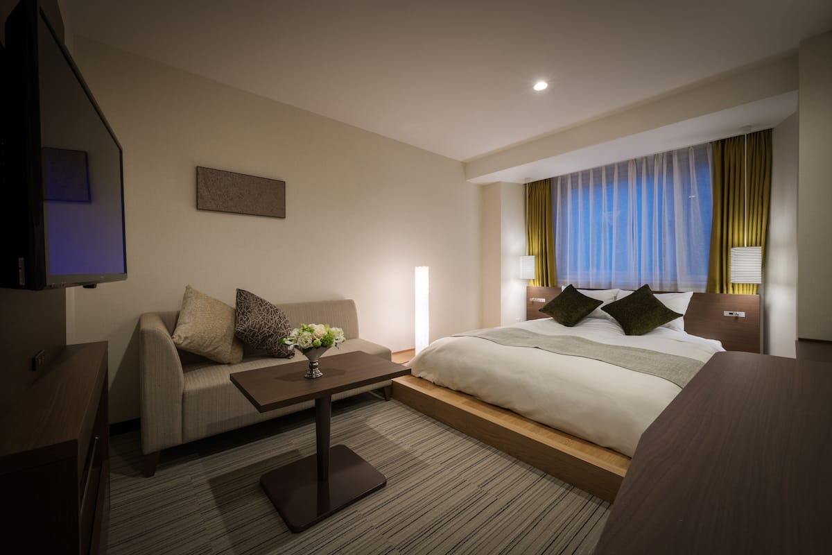 A hotel room with a bed, a sofa, a coffee table, and a TV.