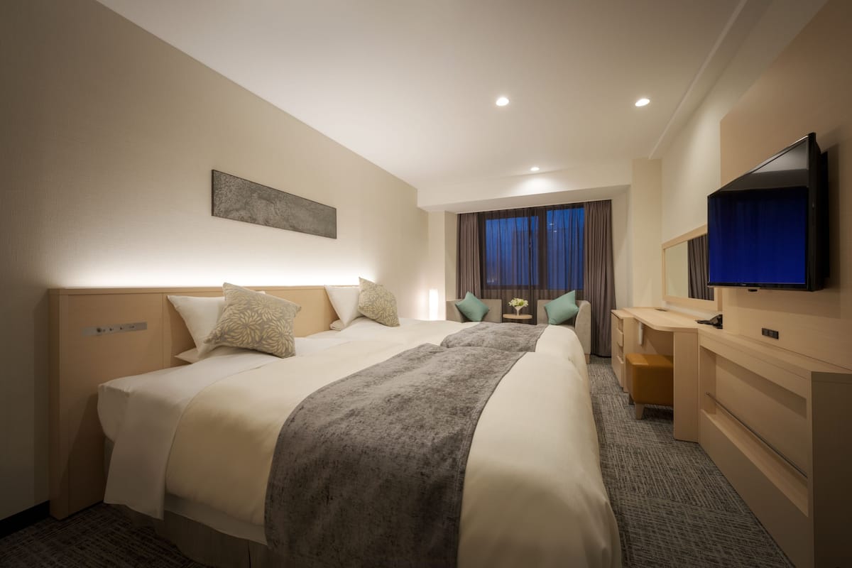 A hotel room with a large bed, a desk, a television, and a window with curtains.