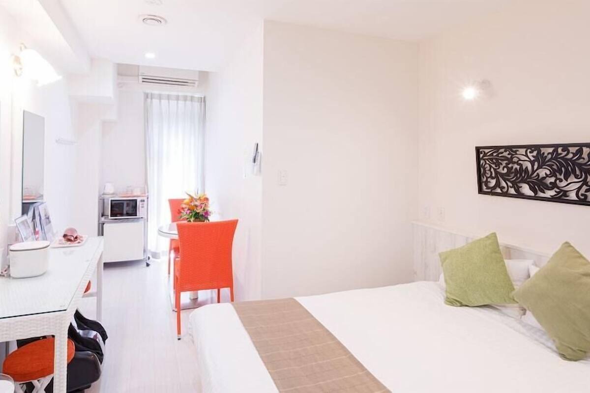 A hotel room with a bed, a desk, a chair, a mirror, and a dining area.