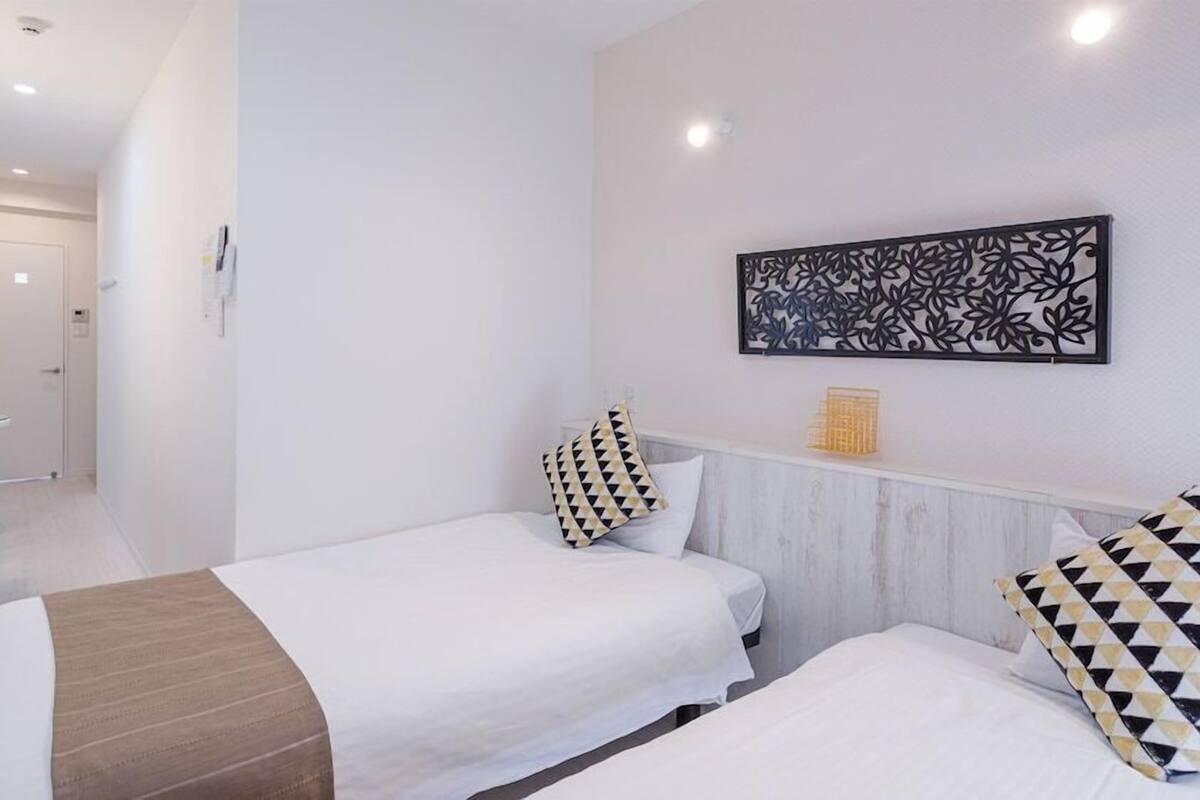 A hotel room with two beds, a desk with a mirror, a small table with a bowl of fruit, and a decorative wall piece.