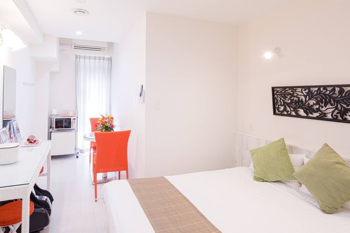 A hotel room with a bed, a desk, a chair, a microwave, and a dining area.