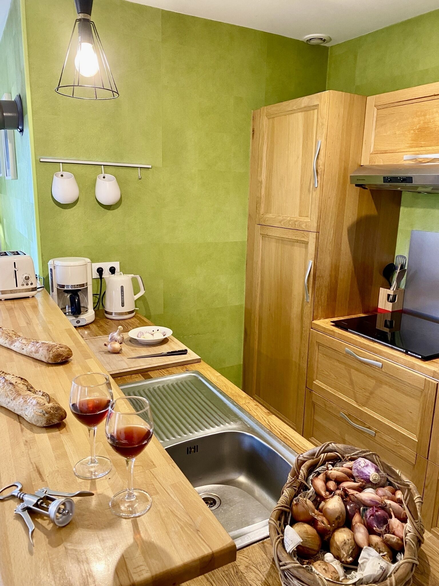 Una cocina con encimera de madera, un fregadero, un tostador, un hervidor y una cesta de cebollas.