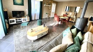A living room with a TV, sofa, ottoman, and a dining area with chairs and a table. - La Villa Mellifera (Cernay-lès-Reims)