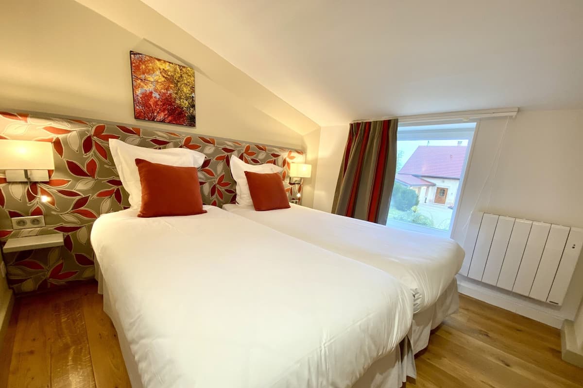 A hotel room with two beds, a leaf-patterned headboard, a window with curtains, and a radiator.