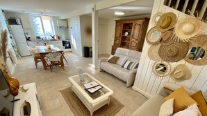 A modern living room with a sofa, coffee table, and decorative hats. A dining area with chairs and a table is visible in the background. - La Villa Mellifera (Cernay-lès-Reims)