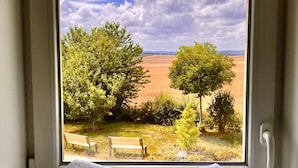 A window view of a garden with two benches and a stack of towels on the windowsill. - La Villa Mellifera (Cernay-lès-Reims)