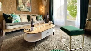 A modern living room with a wooden coffee table, a sofa with green cushions, a green ottoman, and a large window with curtains. - La Villa Mellifera (Cernay-lès-Reims)
