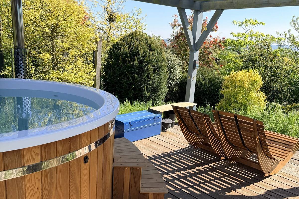 A wooden deck with a hot tub, wooden benches, and a covered area.