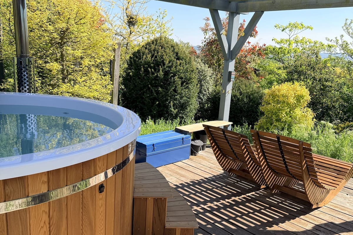 A wooden deck with a hot tub, wooden benches, and a covered area.
