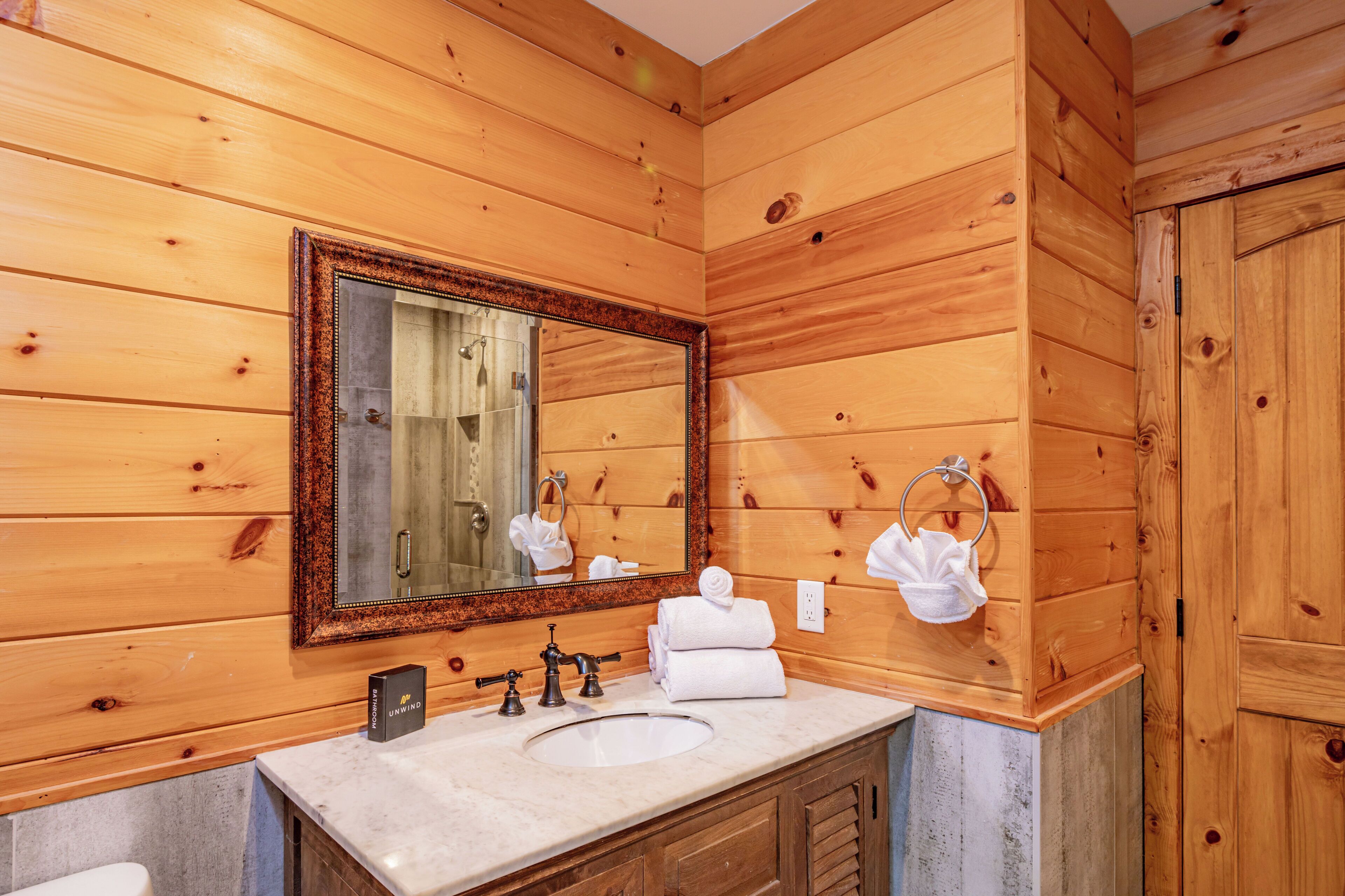 A wooden cabin-style bathroom with a large mirror, a sink with a marble countertop, and wooden cabinets.